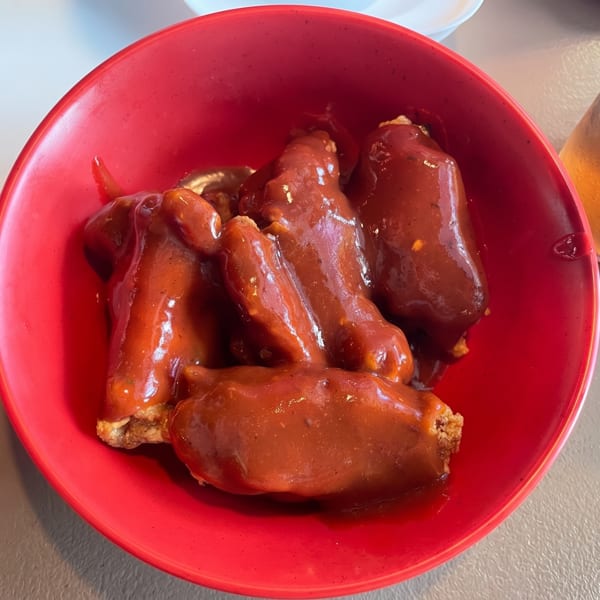 A red bowl filled with several chicken wings generously coated in a rich, dark red sauce.