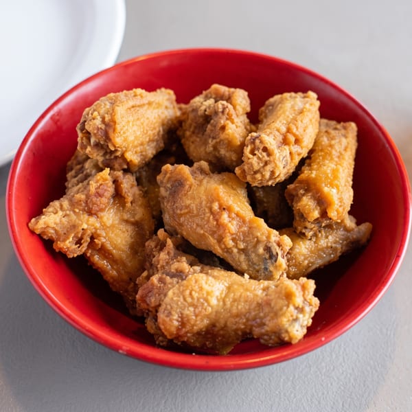 Crispy fried chicken wings in a red bowl, with a glass of beer and a white plate nearby.